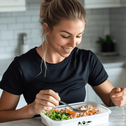 Young woman enjoying a healthy meal prep with vegetables and protein in a kitchen setting.