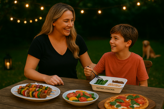 Woman and boy enjoying an outdoor dinner with skewers, salad, and pizza under string lights.